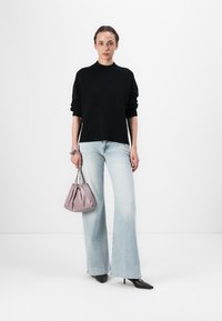 Svart genser, lyseblå vide jeans og svarte høyhælte sko. Holder en liten, myk lavendelveske. Enkelt, rent design.