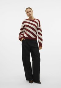 Maglione in lana a righe rosse e crema, con vestibilità ampia, scollo rotondo e spalle scese, abbinato a pantaloni neri a gamba larga con vita alta.