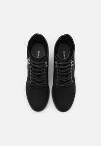 Černé nubukové kotníkové boty s kovovými očky, plochými tkaničkami, kulatou špičkou a texturovanou podrážkou pro lepší přilnavost. Minimalistický design, bez ozdob.