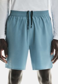 Pantalones cortos deportivos azules hechos de tela ligera, con una cintura elástica y cordón negro, cortes laterales y un acento de logo.