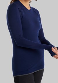 Námořnická modrá fitted dlouhá kůže s texturovanou tkaninou, otvory na palce v manžetách a zaobleným výstřihem. Disponuje hladkým lemem a elastickým materiálem.