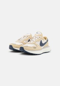 Beige suede and mesh sneakers with a white midsole, navy accents, and textured outsole. Features a prominent Nike logo on the side.