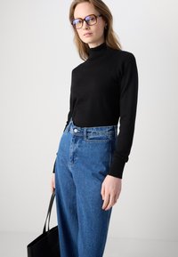 Svart polotröja i kombination med högmidjade blå denimjeans. Tröjan har en figurnära design; jeansen är lösa med knappstängning.