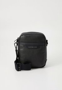 Must tekstureeritud kunstnahast üleõlakott, millel on ees logoplaat, tõmbluku kinnituse ja reguleeritav rihm. Kompaktne ristkülikukujuline disain.