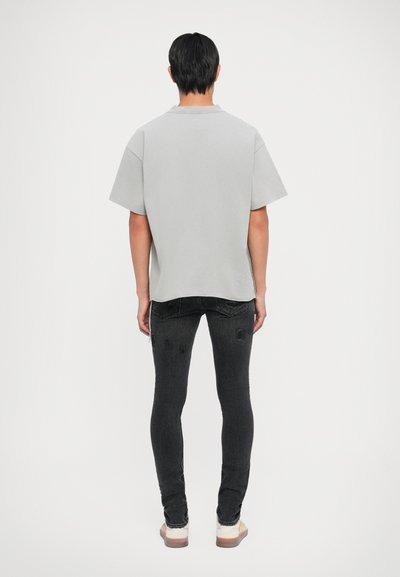 Grå kortermet polo skjorte, bomullsblanding, avslappet passform, brukt med svarte slitte skinny jeans og beige sko, sett fra baksiden.