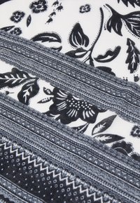 Motifs floraux et géométriques noirs disposés en bandes horizontales sur un fond de tissu blanc.