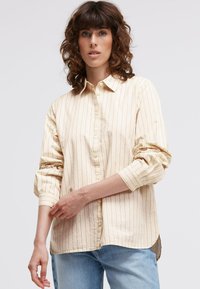 Beige button-up shirt with vertical dark stripes, rolled sleeves, classic collar, and a curved hem, made of soft, textured fabric.