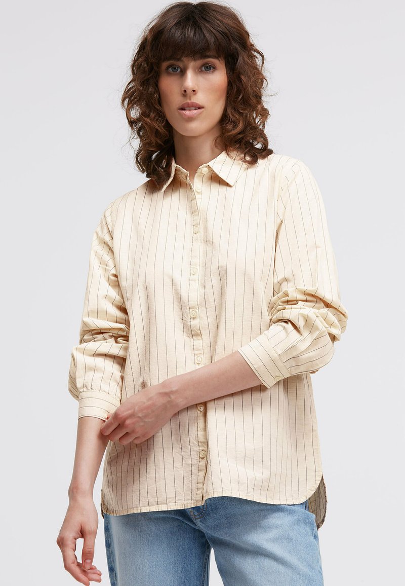 Beige button-up shirt with vertical dark stripes, rolled sleeves, classic collar, and a curved hem, made of soft, textured fabric.