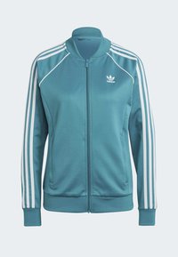 Tyrkysová sportovní bunda se zipem vpředu, bílým logem Adidas a třemi bílými pruhy na každém rameni a rukávu, vyrobená z hladkého materiálu.