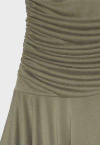 Section de robe vert olive avec tissu froncé à la taille et jupe lisse et fluide en dessous.