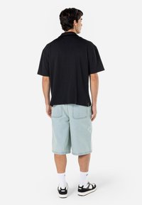 Maglietta nera a maniche corte, tessuto strutturato, vestibilità comoda, abbinata a pantaloni corti di jeans azzurri, calze bianche e sneaker nere.