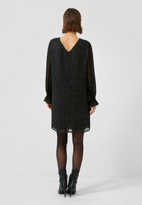 Czarna sukienka z teksturowanym gorsetem i przezroczystymi długimi rękawami. Posiada dekolt w kształcie litery V na plecach oraz koronkową lamówkę na dole. Ubrana z czarnymi botkami do kostki.