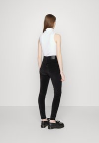 Calças de veludo cotelê pretas de cintura alta com um corte ajustado e textura suave em relieve, combinadas com uma blusa branca sem mangas e calçado preto.