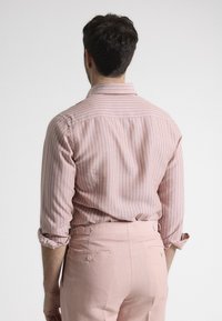 Camisa de rayas rosa claro con mangas enrolladas, hecha de una tela suave, combinada con pantalones entallados rosa claro que cuentan con bolsillos laterales.