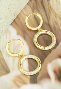 Guld-hoopörhängen med en slät yta, i en cirkulär form och med en sektion prydd med små, glittrande rhinestones.