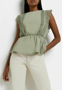Světle zelený peplum top s krajkovým zakončením, kulatým výstřihem a krátkými letními rukávy, v kombinaci s krémovými kalhotami.