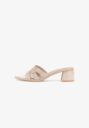 Beige mule sandaal met open teen, gevlochten leren bandjes en een lage, brede hak op een witte achtergrond.
