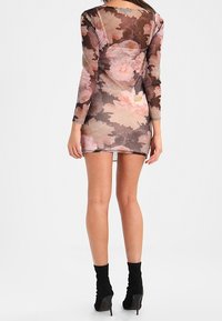 Průhledné šaty s květinovým vzorem, dlouhými rukávy, propracovaným střihem a výstřihem na zádech, v tlumených růžových a hnědých odstínech.
