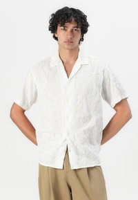 Short-sleeve white shirt with textured floral embroidery and a notched collar, featuring a button-down front and relaxed fit.
