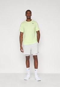 T-shirt Nike vert clair et short gris clair. Le mannequin porte des chaussures de sport blanches et des chaussettes montantes avec le logo Nike. Design simple, sans motifs.
