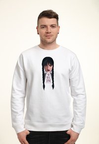Uomo che indossa un felpa bianca con grafica di una donna con trecce nere e la scritta "No Hug Zone" sul davanti.