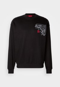 Sweat-shirt noir à manches longues avec poignets et ourlet côtelés, présentant un motif cachemire et toile d'araignée blanc et un texte rouge "HUGO" sur la poitrine gauche.