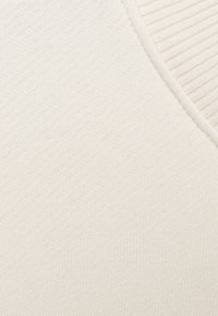 Tissu beige clair avec une texture côtelée et une finition lisse, présentant un décolleté en V et un matériau doux et extensible.