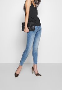 Černá krajková cami, modré slim-fit džíny s bočními knoflíky, hnědé hadí lodičky a strukturovaná černá kabelka.