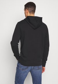 Czarna bluza z kapturem o gładkiej fakturze, ze ściągaczami na mankietach i regulowanym sznurkiem. Noszona z niebieskimi jeansami, prezentując casualowy styl.