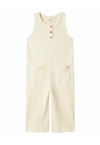 Une combinaison en ribbed couleur crème avec un col rond, des boutons en bois et deux poches avant. Jambes courtes avec un ourlet légèrement festonné.