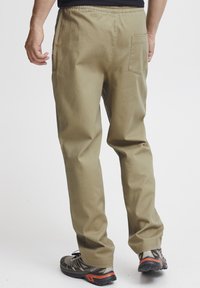 Khaki cotton pants with an elastic waistband, featuring a back pocket, straight leg design, and a smooth texture. Paired with gray sneakers.