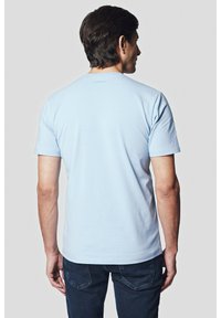 Jasnoniebieska bawełniana koszulka z krótkim rękawem i okrągłym dekoltem. Prosty wzór, bez widocznych wzorów czy akcentów, noszona z ciemnoniebieskimi dżinsami.