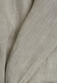Gros plan sur un tissu en lin beige clair avec une texture de tissage visible et des plis doux.