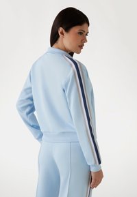  Lichtblauwe zip-up jas met een geribbelde kraag en manchetten, voorzien van witte en marineblauwe strepen langs de mouwen. Glad materiaal, losse pasvorm.