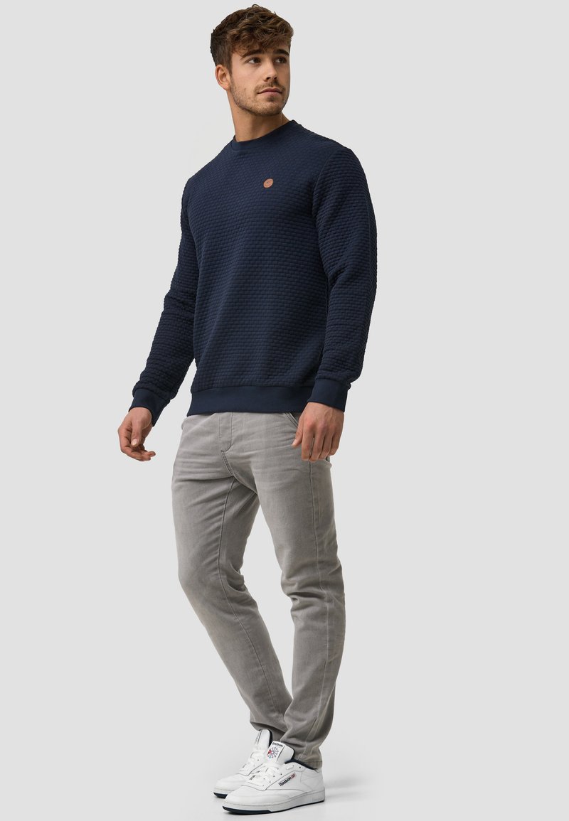 Marineblauwe sweatshirt met textuur, voorzien van een ronde halslijn en geribbelde manchetten, gecombineerd met lichtgrijze slim-fit broek en witte sneakers.