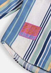 Chemise en coton rayée avec des motifs bleu, vert et blanc. Comprend une étiquette en tissu rose avec un design floral et un logo "Oxbow".