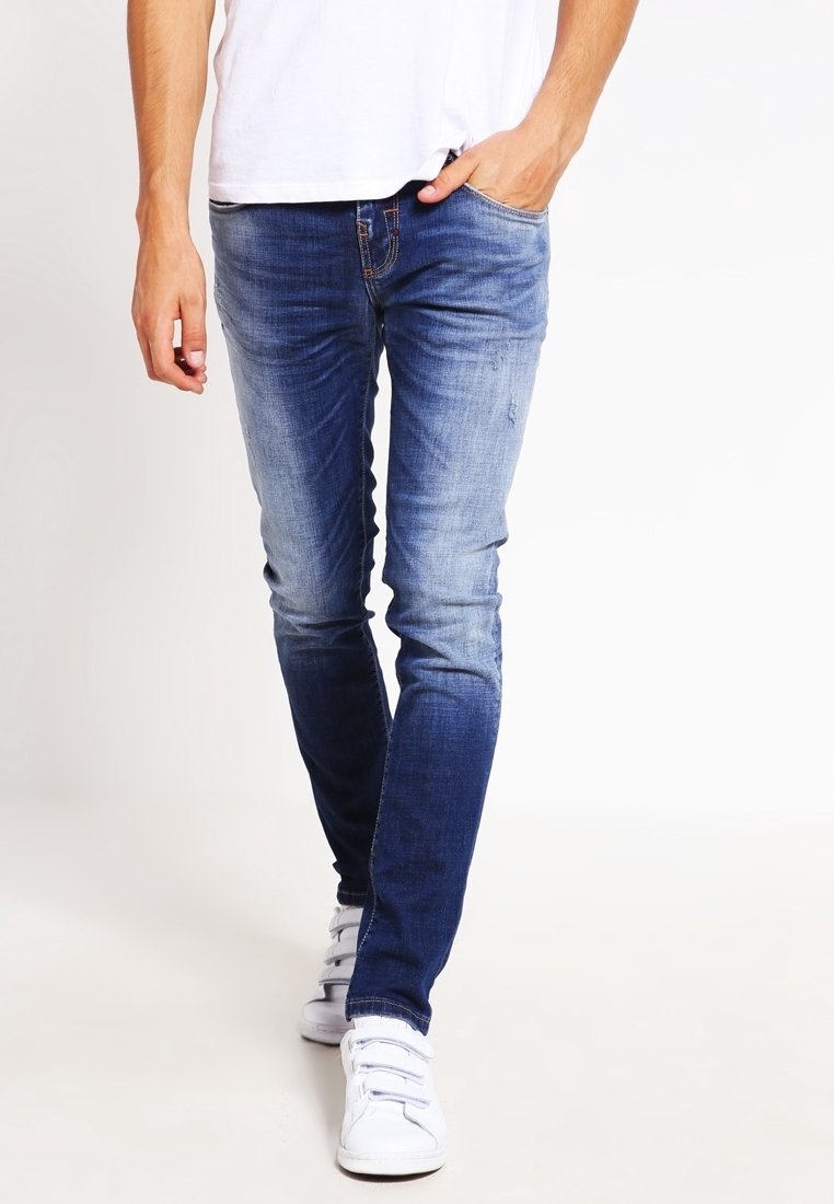 Smala blå jeans, urtvättade vid låren; gjorda av denim med en slät textur, kombinerat med vita sneakers, visade i en gående pose.