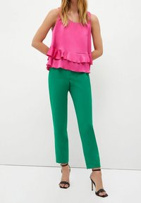 Rosa ärmlös topp med volangkant i kombination med figurnära gröna byxor. Klädseln kompletteras av svarta remsandaler med hög klack.