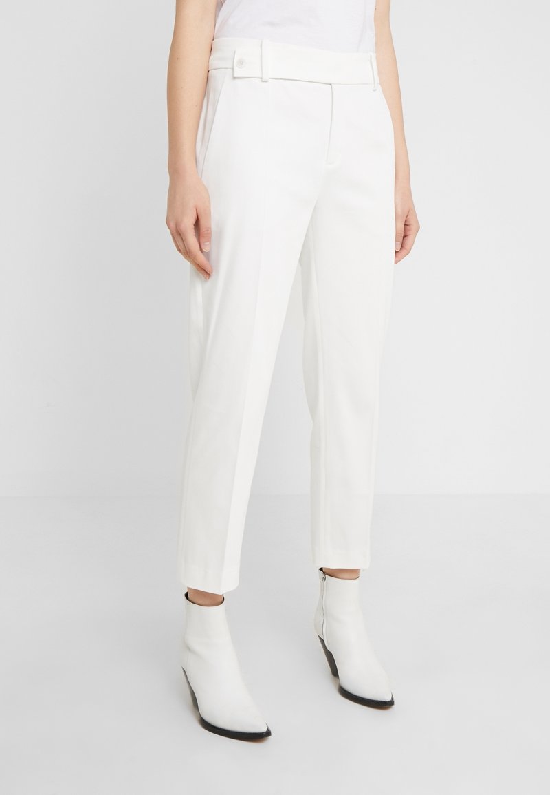 Białe dopasowane spodnie z prostą nogawką, z szerokim paskiem w talii i zapięciem na guzik. W połączeniu z białymi botkami za kostkę.