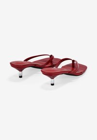 Sandalias rojas de suela plana con tiras finas y diseño de punta cuadrada. Tacones cortos, transparentes y con acentos negros. Textura suave y brillante.
