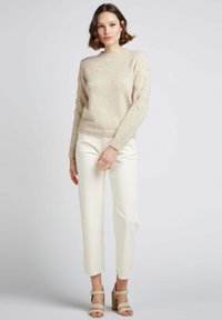 Pull beige avec des détails texturés sur les épaules, associé à un pantalon blanc cropped et des escarpins beiges à bride cheville. Tissu lisse et coupe décontractée.