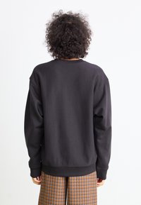 Zwarte oversized sweatshirt met ribbeltonden ronde hals en manchetten, gladde textuur, gedragen met bruine geruite broek met blauwe lijnen.
