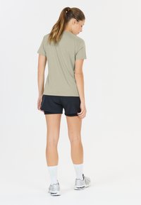 Lichtgrijs, kortemouwen shirt gecombineerd met zwarte sportshorts. Het model draagt witte sokken en zilveren hardloopschoenen, met de rug naar de camera gekeerd.
