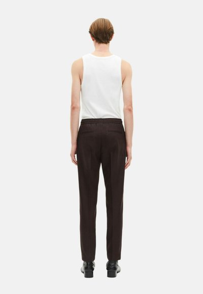 Achteraanzicht van een persoon in een witte tanktop en bruine broek met een relaxte pasvorm, voorzien van een elastische tailleband en zijzakken.