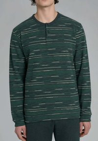 Maglietta verde a maniche lunghe con strisce bianche orizzontali, scollo tondo, due bottoni e polsini a costine. Il tessuto sembra morbido e strutturato.