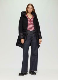 Zwarte pufferjas met capuchon, rood-wit gestreept henley shirt, hoge taille donkerdenim wijde broek en zwarte chunky laarzen.