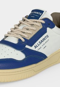 Άσπρο και μπλε sneaker AllSaints με μπεζ κορδόνια, υφασμένο δέρμα και κείμενο με την επωνυμία στα αγγλικά και ιαπωνικά στην πλευρά και στη γλώσσα.
