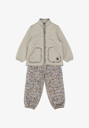 Pihe-puha bézs dzseki két első zsebbel és magas nyakkal; mintás világos nadrág, amely különféle állatokat ábrázol tompa színekben.