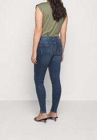 Jeans ajustados de cintura alta en azul, con un diseño tradicional de cinco bolsillos, un ligero desvanecimiento y un sutil detalle de corte en el tobillo.