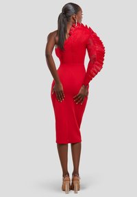 Rød kjole med én skulder af blonder og én flæseærme, tætsiddende silhuet, knælængde, med et slids bagpå og båret med klare hæle.